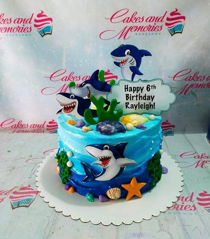 Blue ocean themed Baby Shark birthday cake with shark printouts, edible seashells, and coral decorations.