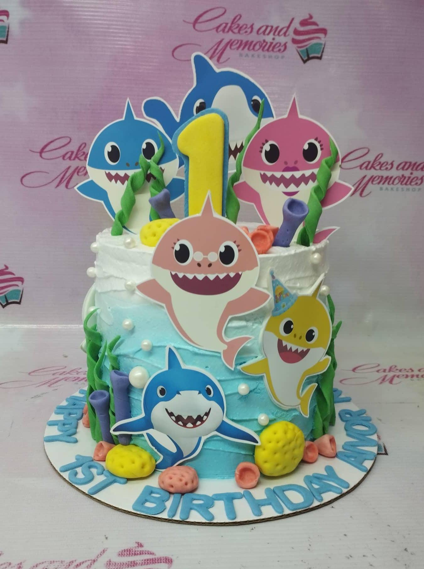 Baby Shark themed 1-tier birthday cake with blue and white textured icing, featuring colorful shark printouts and fondant sea decorations.