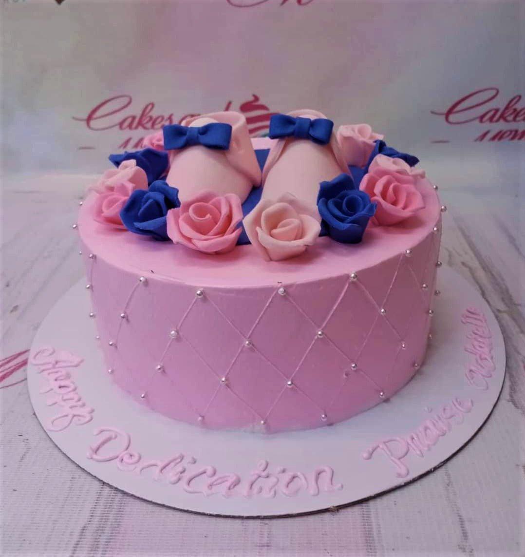 Pink baby shoes cake with pink and blue edible roses and silver dragees on a quilted icing pattern.