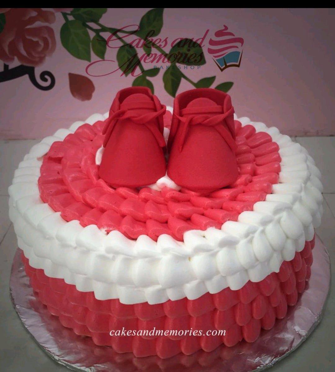 Red and white 1-tier cake with piped icing ruffles and red fondant baby shoes on top.