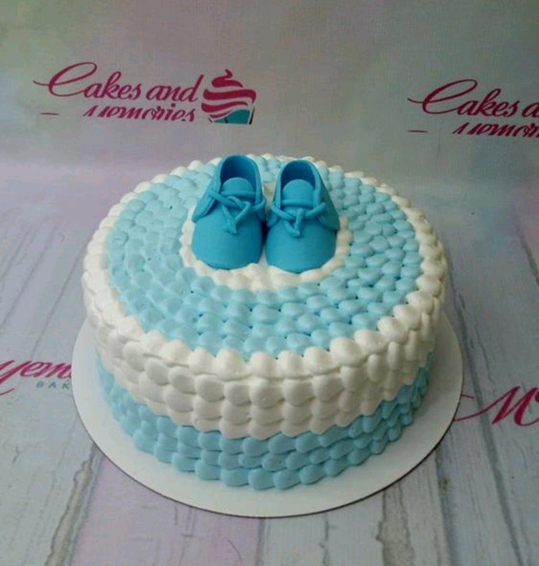 Blue and white soft icing cake with piped petal texture and blue fondant baby shoes on top.