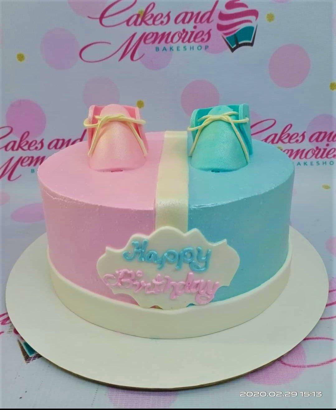 Pink and blue gender reveal or birthday cake with fondant baby shoes and a Happy Birthday message.