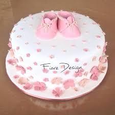 White fondant cake decorated with pink and peach gumpaste flowers and a pair of pink baby booties on top.