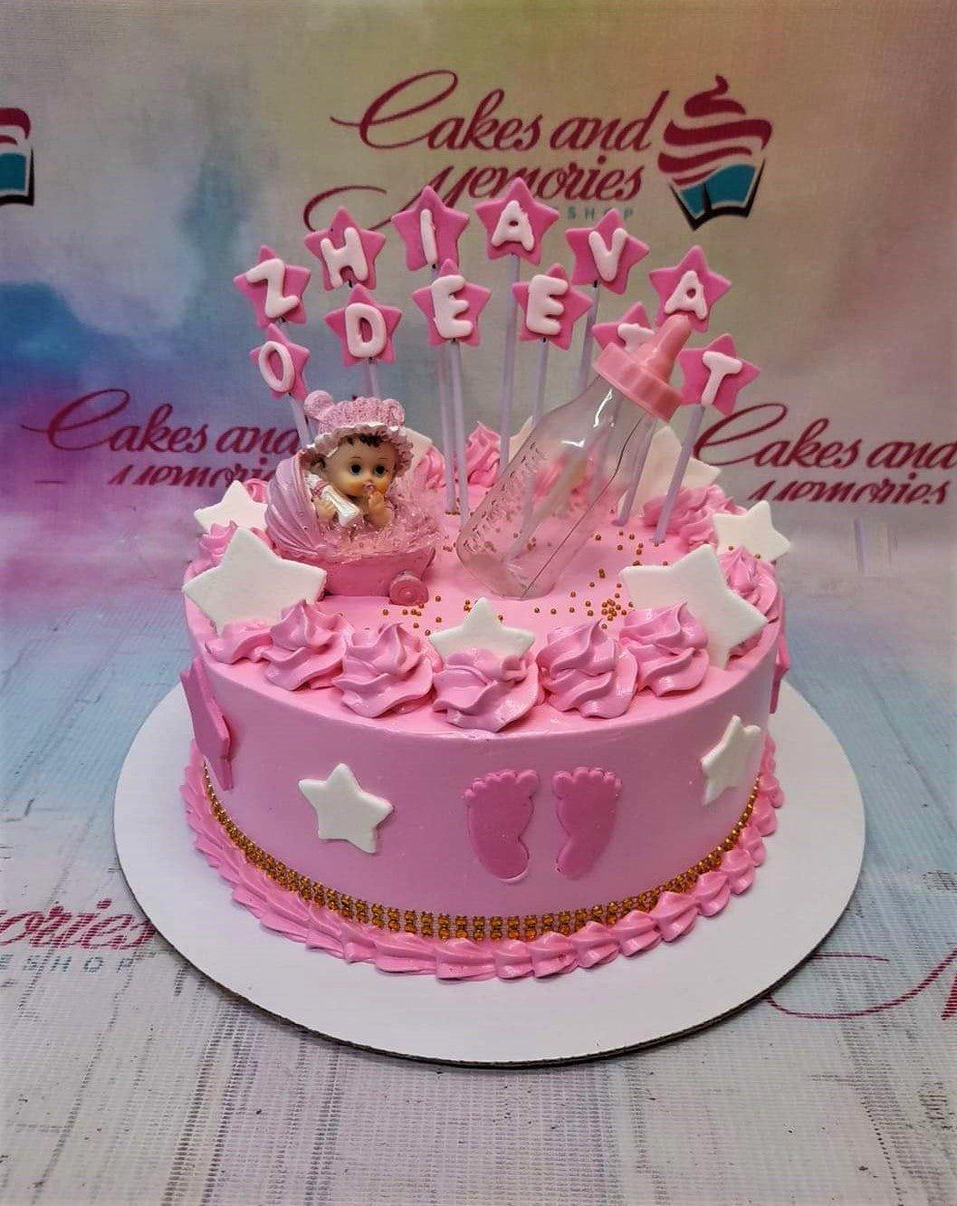 Pink baby shower cake with a fondant baby in a stroller, a baby bottle topper, and pink icing rosettes.