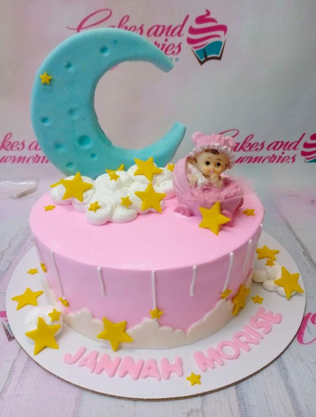 Pink baby shower cake with a large blue crescent moon, yellow stars, white clouds, and a baby in a pink stroller topper.