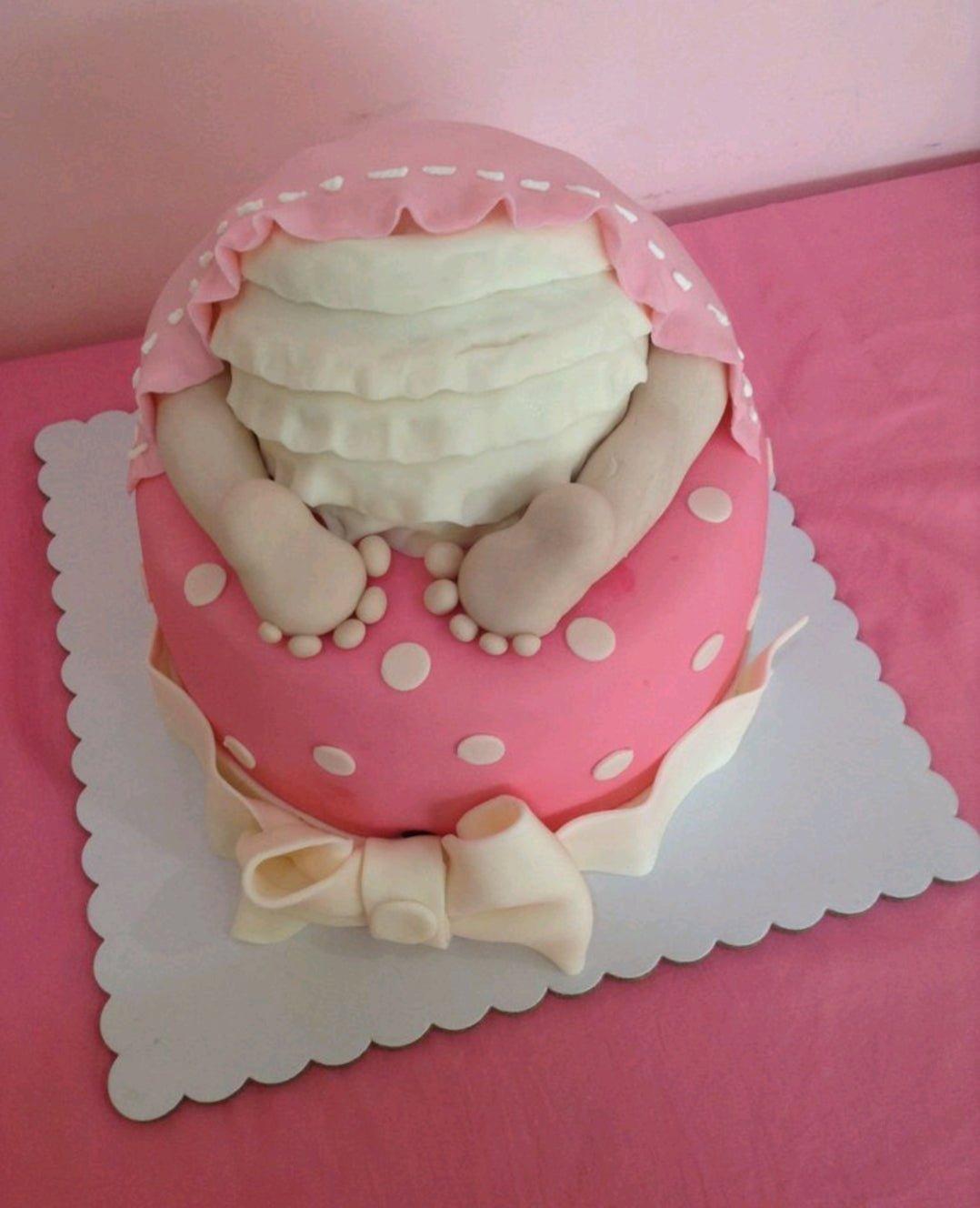 Pink fondant baby shower cake featuring a 3D fondant baby bottom with ruffles and a large white bow.