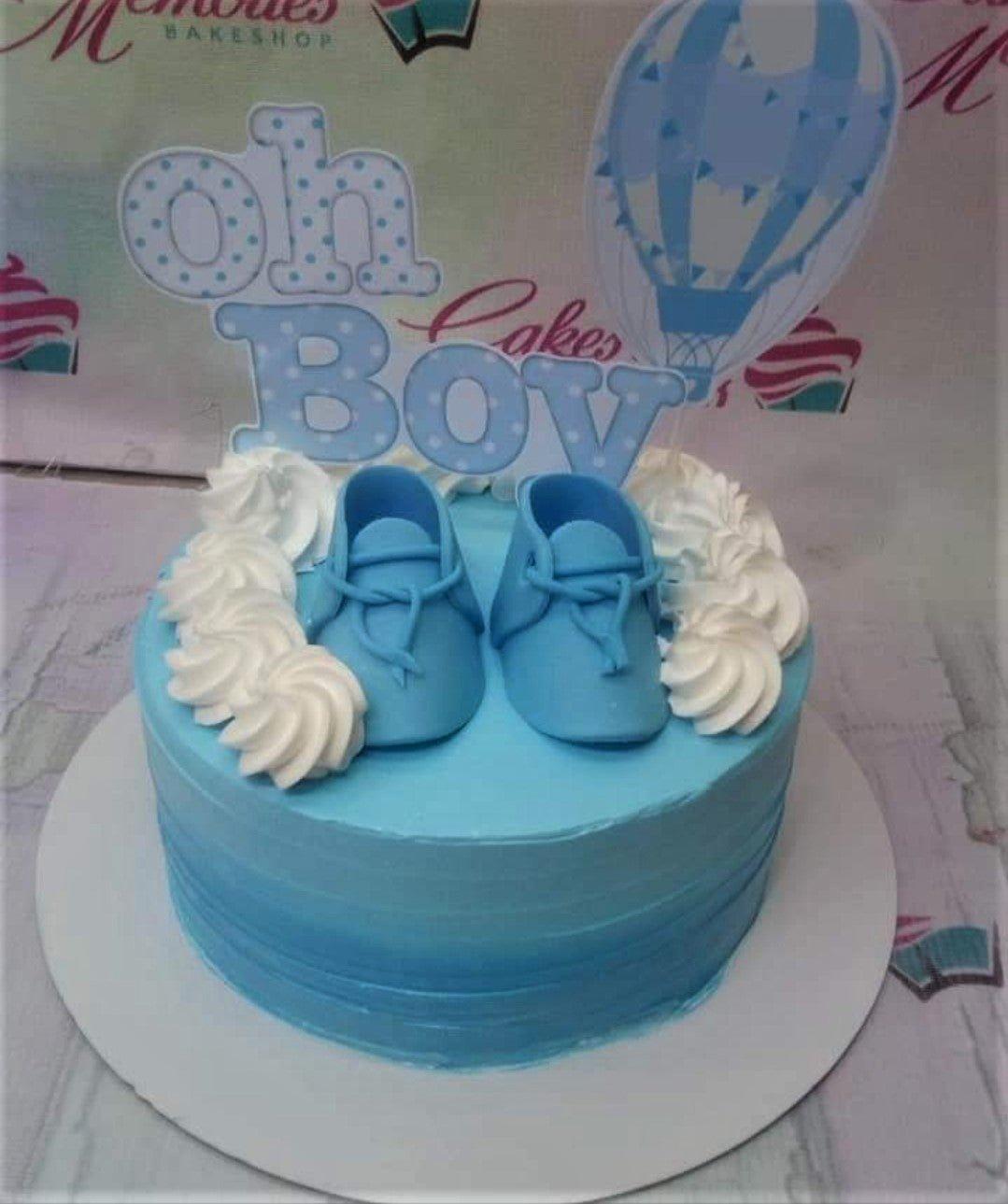 Light blue 1-tier baby shower cake with fondant baby shoes, white icing swirls, and a hot air balloon printout topper.