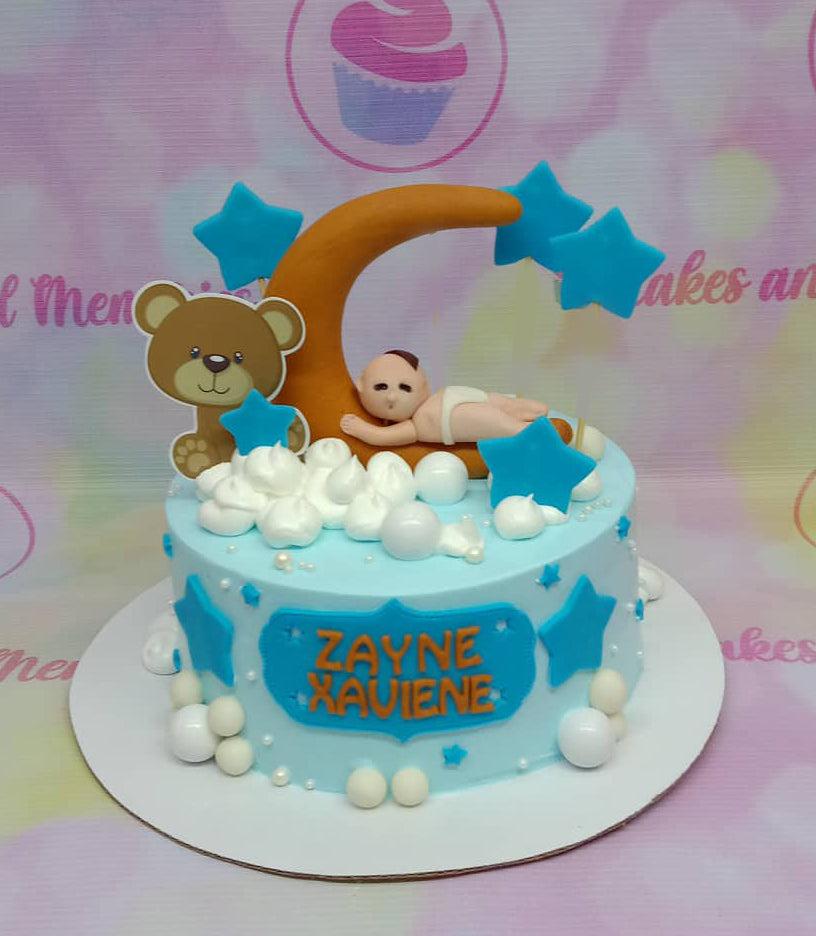 Light blue baby shower cake with a fondant sleeping baby on a crescent moon, teddy bear printout, and white meringue clouds.