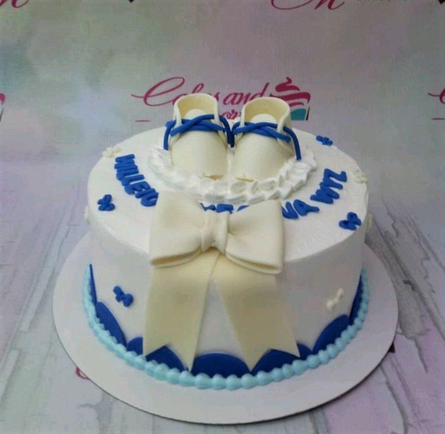 White and blue baby shower cake with fondant baby shoes and a large white bow.