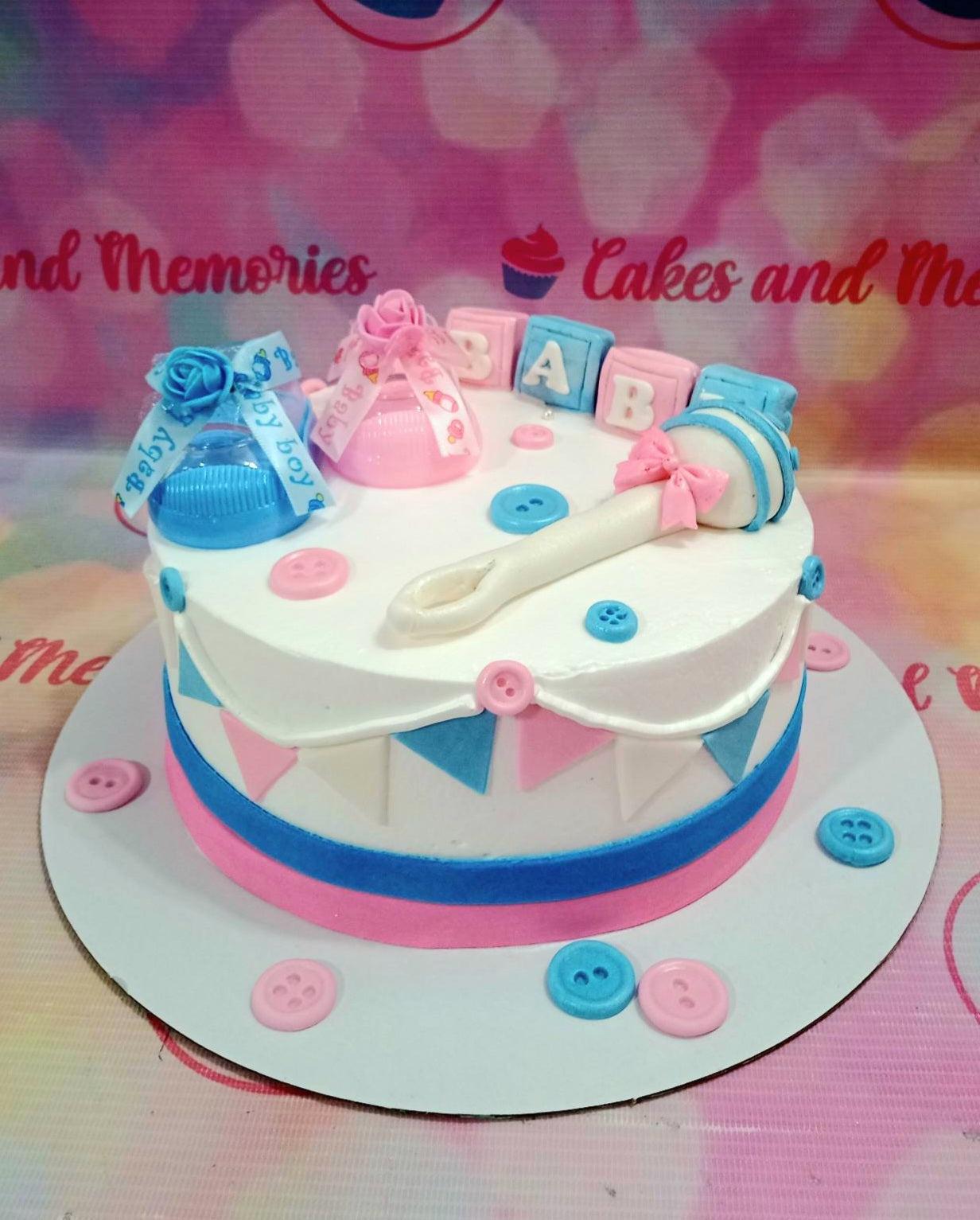 Blue and pink baby shower cake with fondant baby bottles, rattle, and alphabet blocks on a white base with bunting decorations.