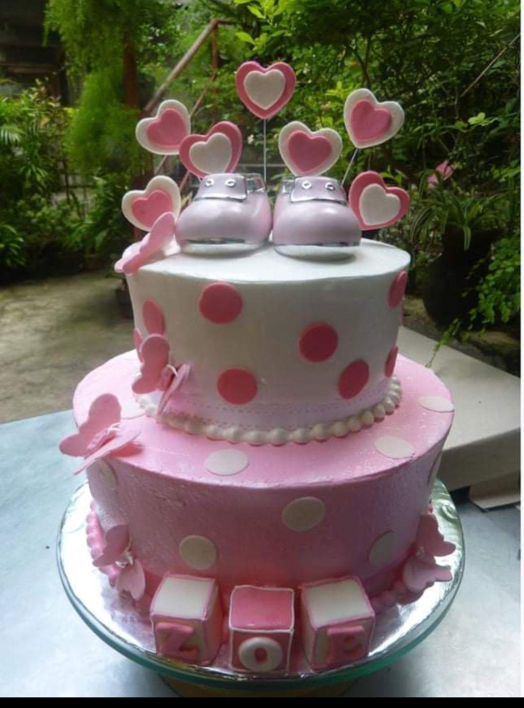 Pink and white two-tier baby shower cake with fondant baby shoes, hearts, and butterflies.
