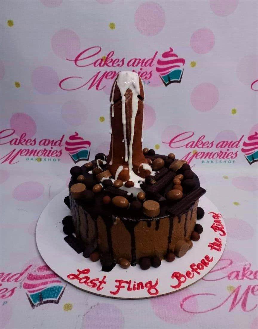 Chocolate drip cake with a brown phallic-shaped fondant topper, chocolate candies, and a bachelorette message on the base board.