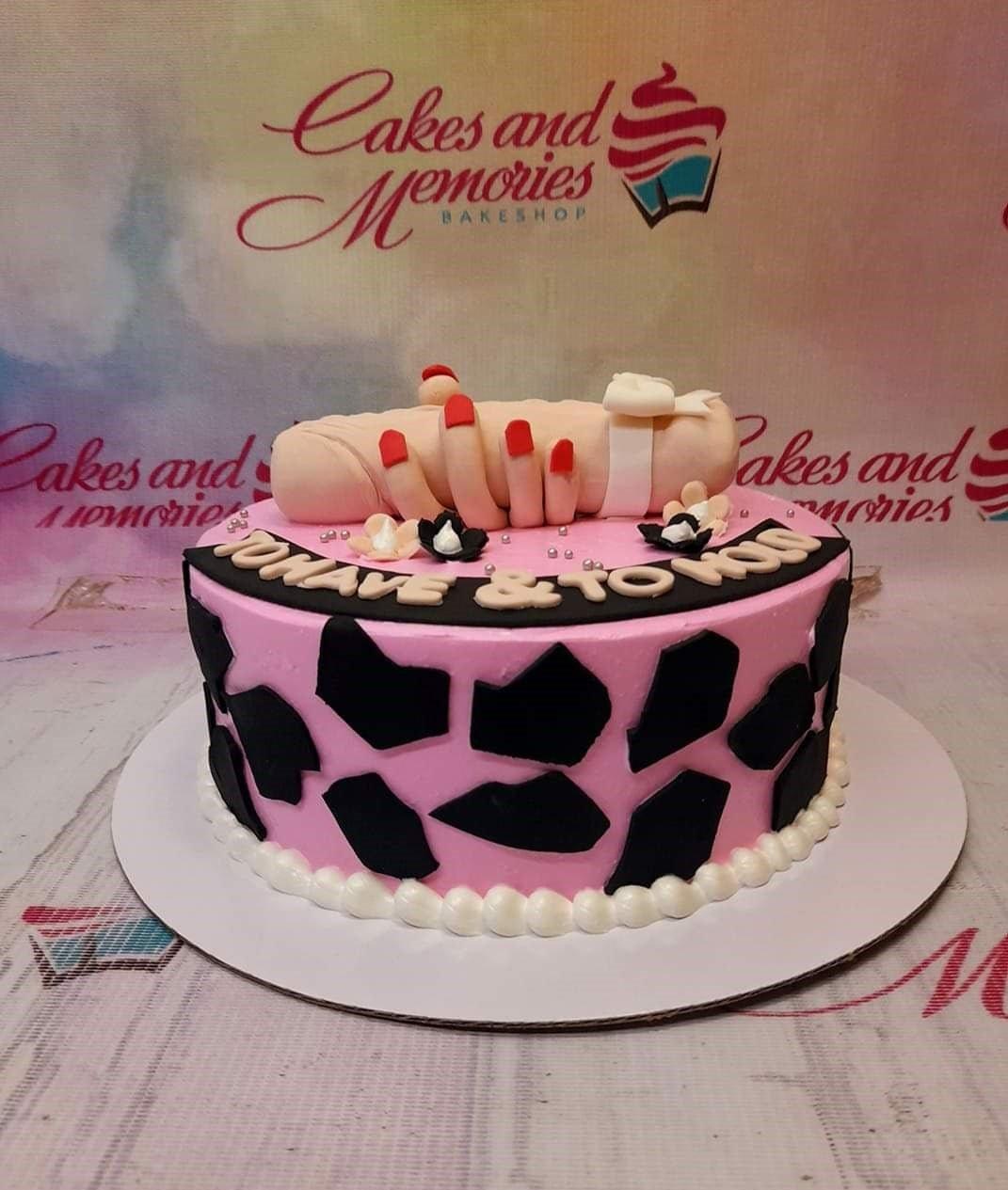 Pink bachelorette cake with black cow print patterns and a humorous 3D fondant hand and phallic topper.