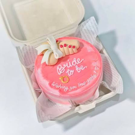 Pink bento cake for a bachelorette party featuring a humorous 3D fondant hand and ring decoration with a playful message.