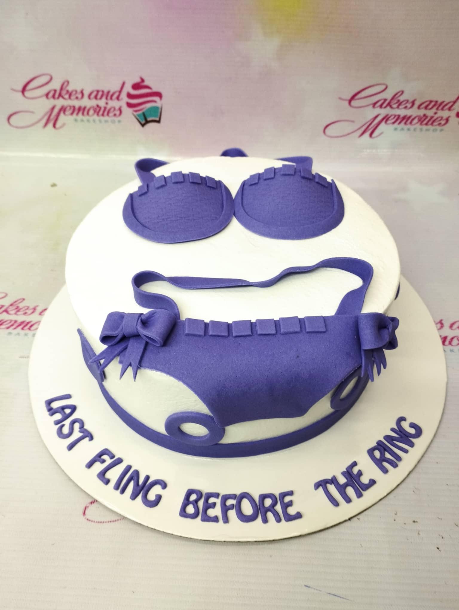 White round cake with purple fondant bikini and lingerie decorations for a bachelorette party.