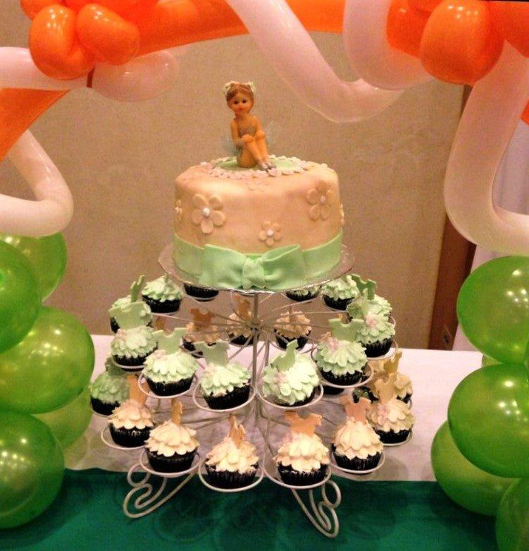 Elegant beige fondant cake with a ballerina topper and matching cupcakes on a white wire stand.