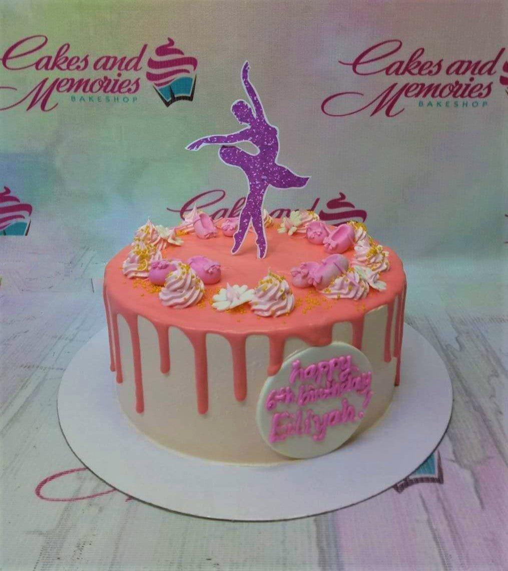 Pink ballerina birthday cake with a purple glitter ballerina topper, pink icing drips, and fondant ballet shoes.