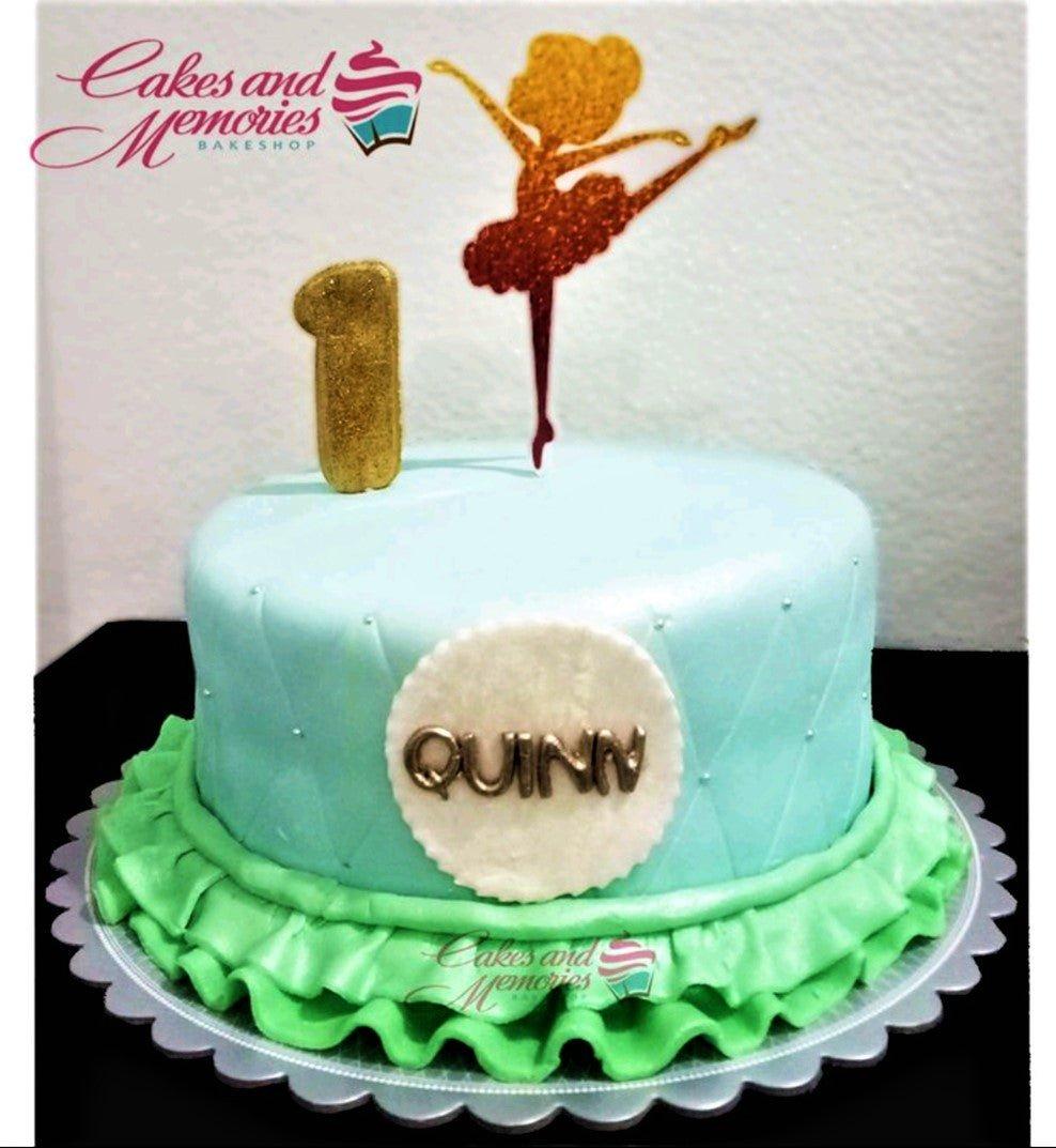 Light blue fondant ballerina cake with a gold glitter ballerina topper, a gold number one, and green ruffles at the base.