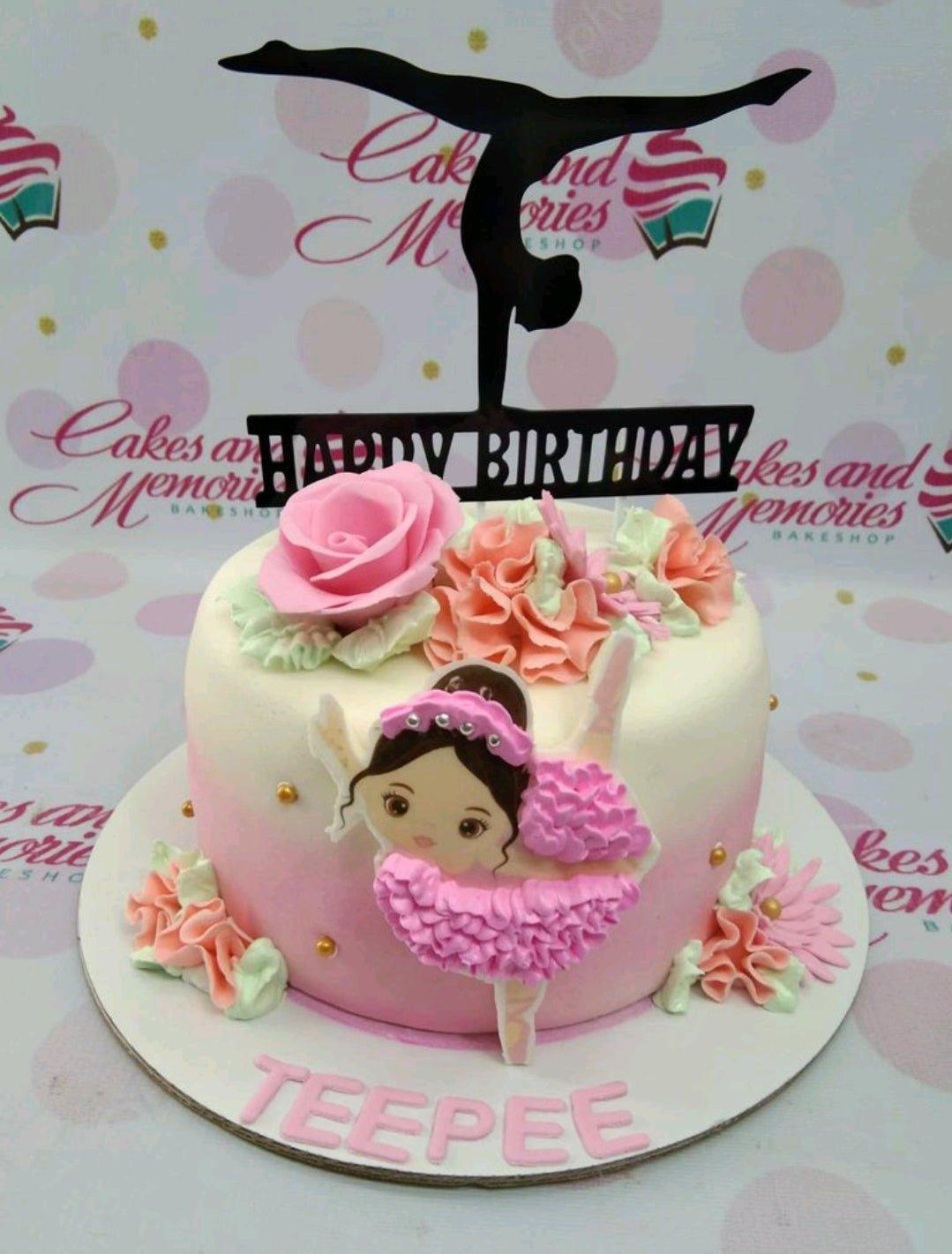 Pink and white gradient ballerina cake with a black gymnast topper, pink icing roses, and a ballerina printout on the side.