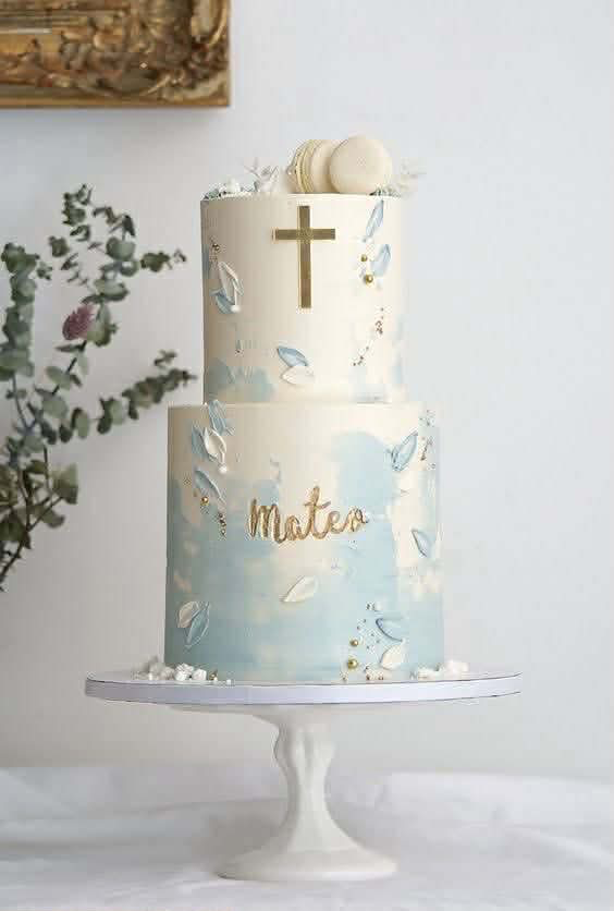 Elegant 2-tier white and light blue baptism cake with a gold cross, macarons, and palette knife icing petals.