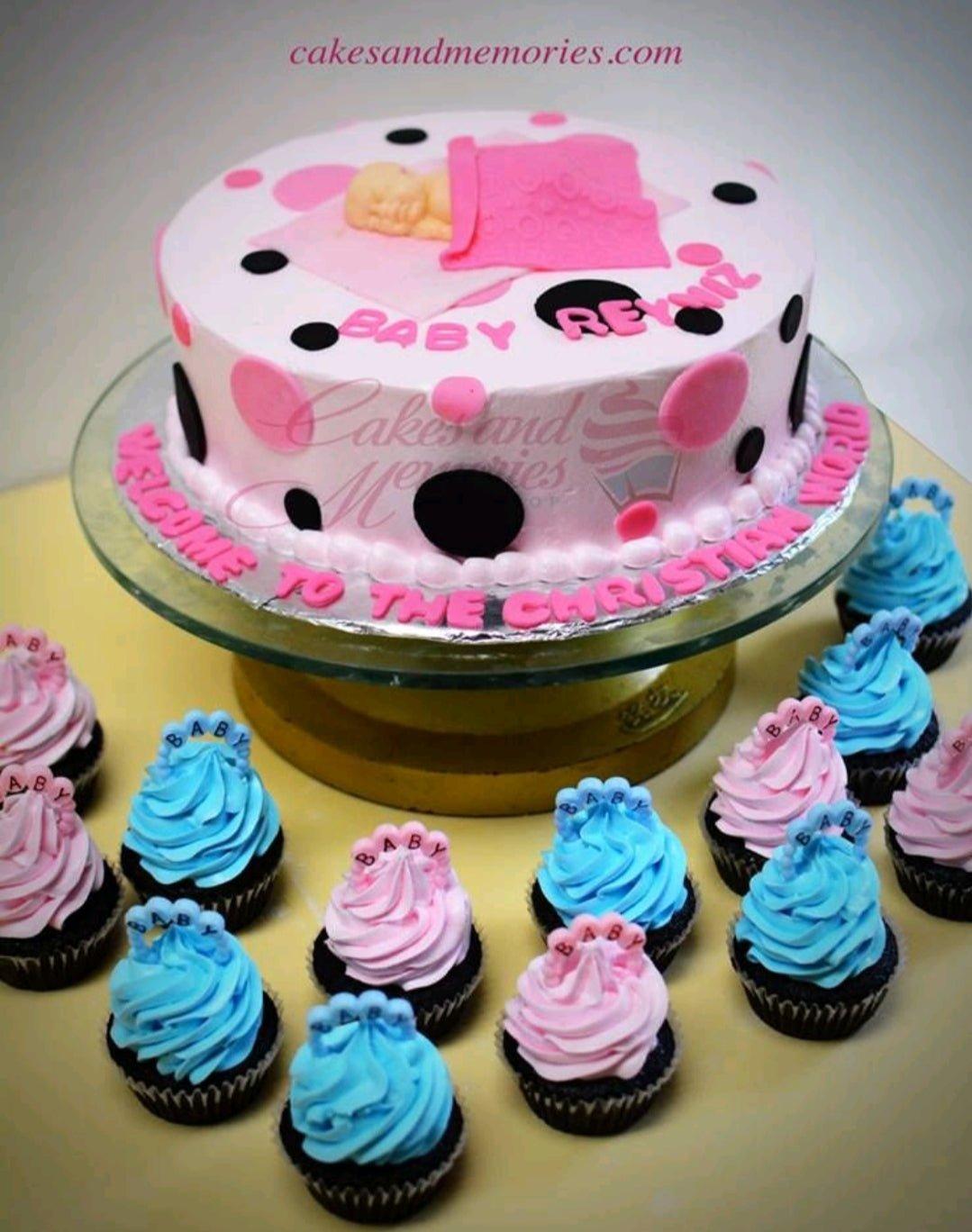 Pink and white baby baptism cake with a sleeping baby fondant topper, black and pink polka dots, and matching cupcakes.