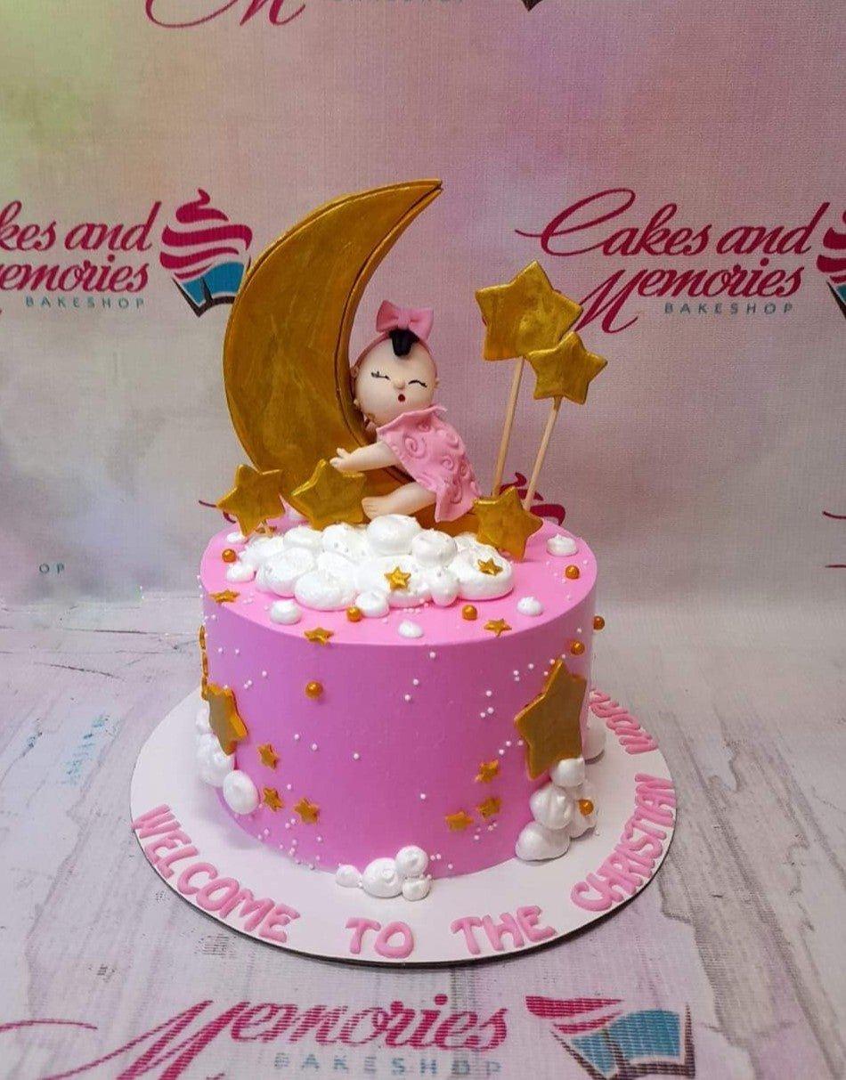 Pink baby girl baptism cake with a fondant baby on a gold moon, white icing clouds, and gold stars.