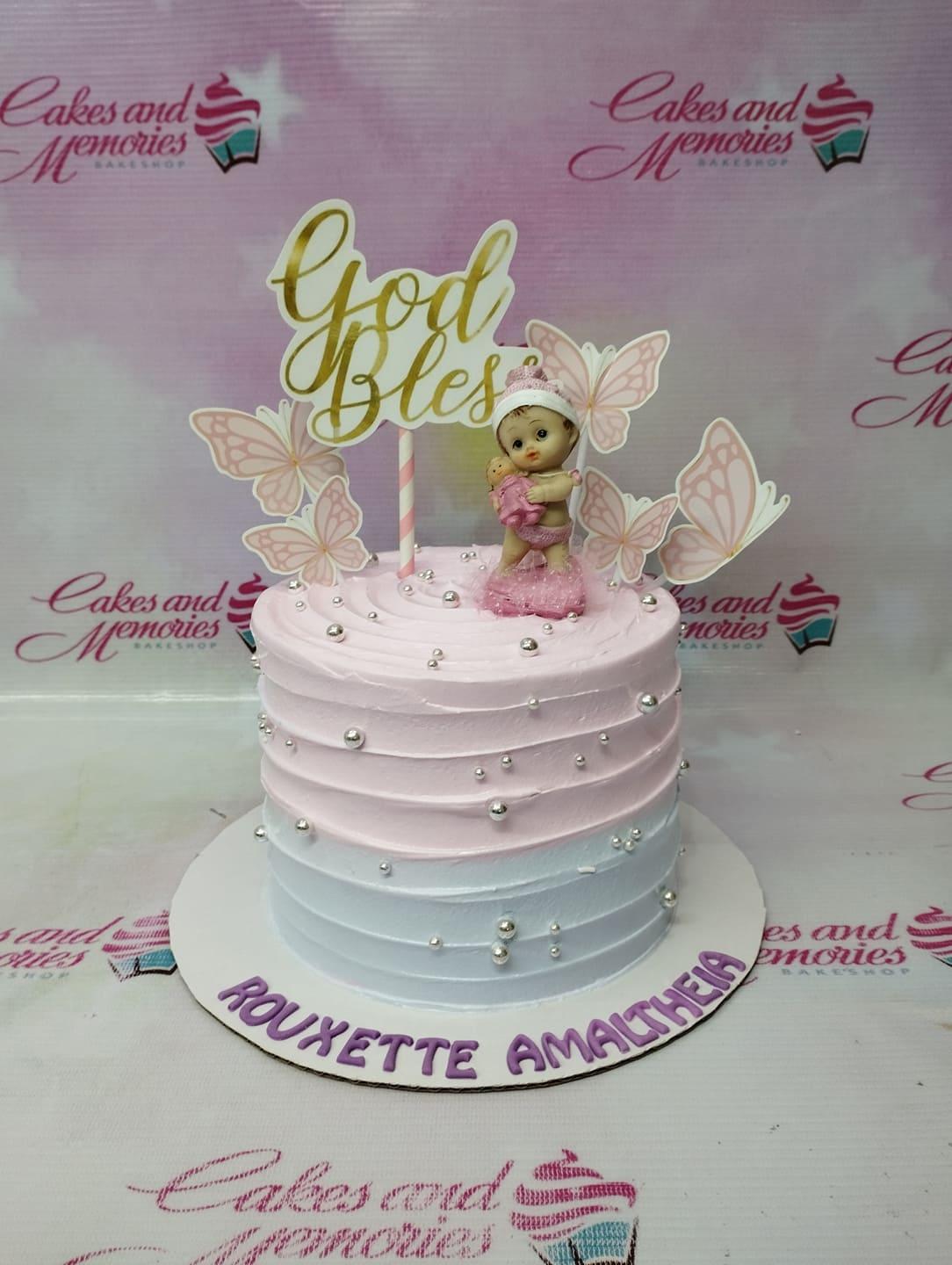 Pink and light blue ombre cake with silver dragees, butterfly printouts, and a baby figurine topper for a baptism or dedication.