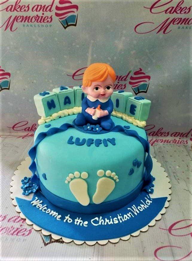 Light blue fondant baby boy baptism cake with a 3D baby figure, alphabet blocks, and white footprints.