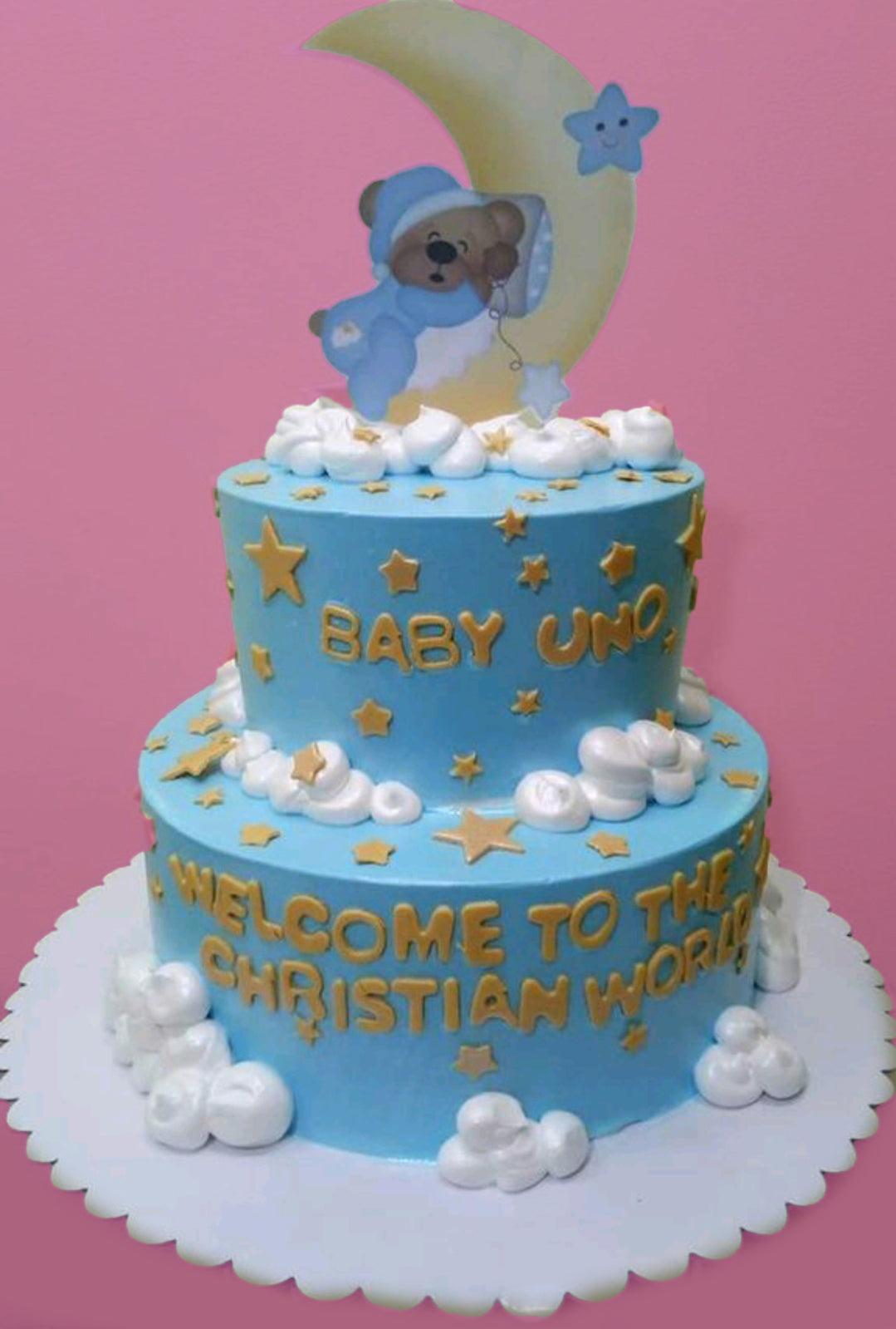 Two-tier light blue baby boy baptism cake with a sleeping bear on a moon topper, white icing clouds, and gold stars.