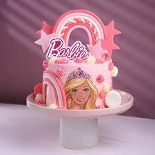 Pink Barbie themed cake with a printed Barbie character, fondant rainbow, and pink stars on a pink cake stand.