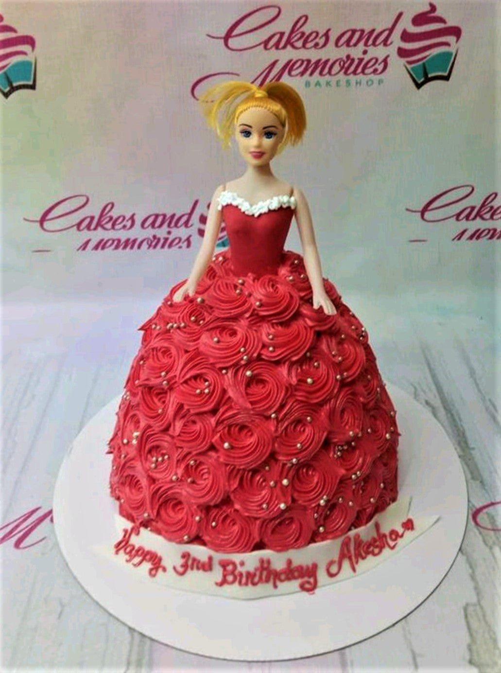 Red Barbie doll cake with a full skirt made of red icing rosettes and silver dragees on a white base board.