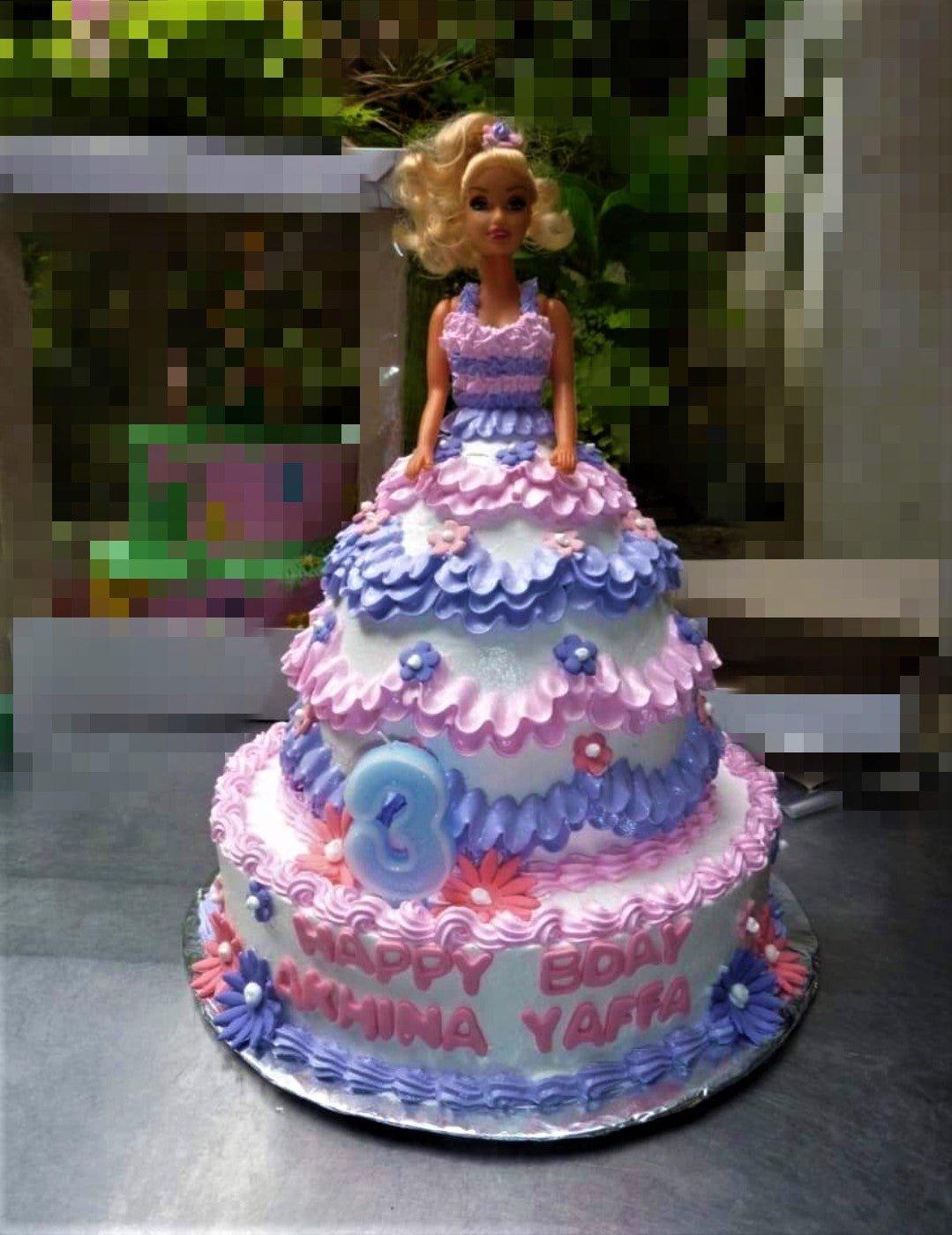 Barbie doll cake with a tiered purple and pink ruffled icing dress and floral decorations.