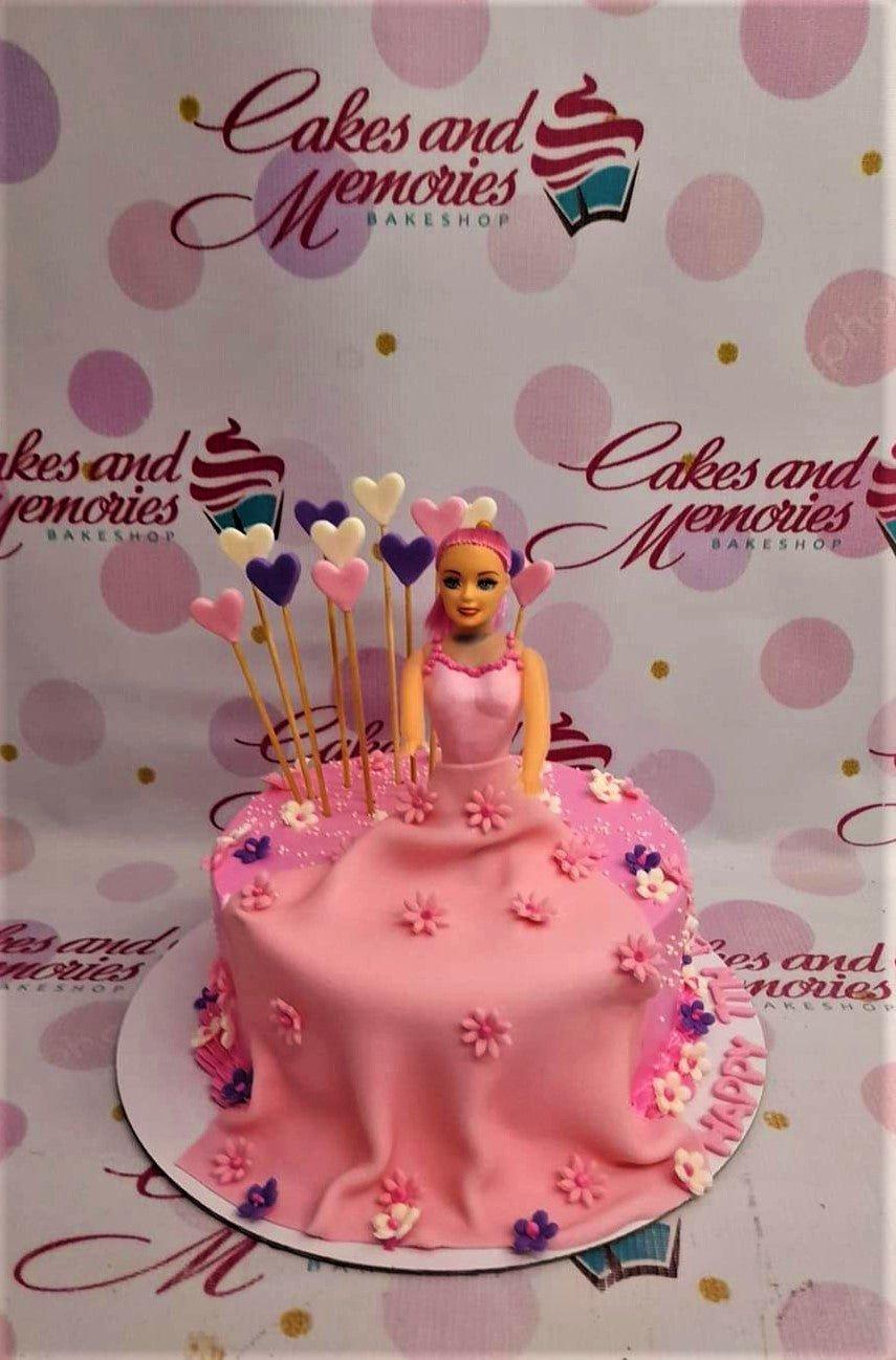Pink Barbie doll cake with a flowing fondant dress decorated with pink and purple flowers and heart toppers.