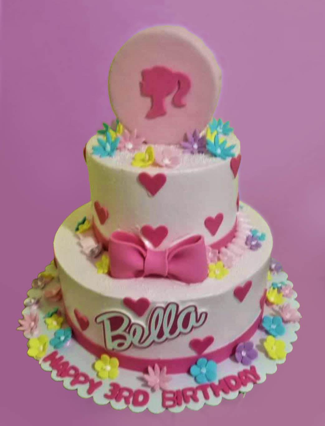Two-tier pink Barbie themed birthday cake with a large pink silhouette topper, fondant hearts, and colorful edible flowers.