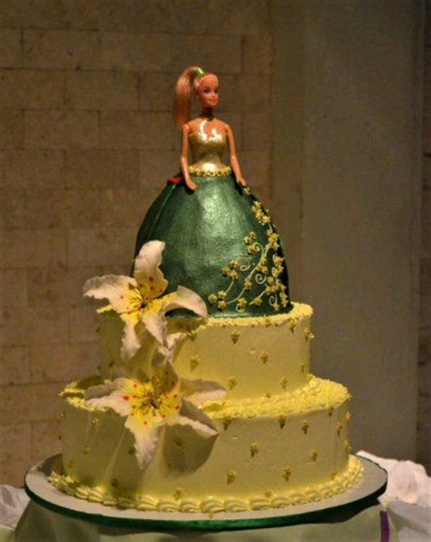 Three-tier Barbie doll cake with a green metallic ballgown skirt and yellow floral accents on light yellow icing.