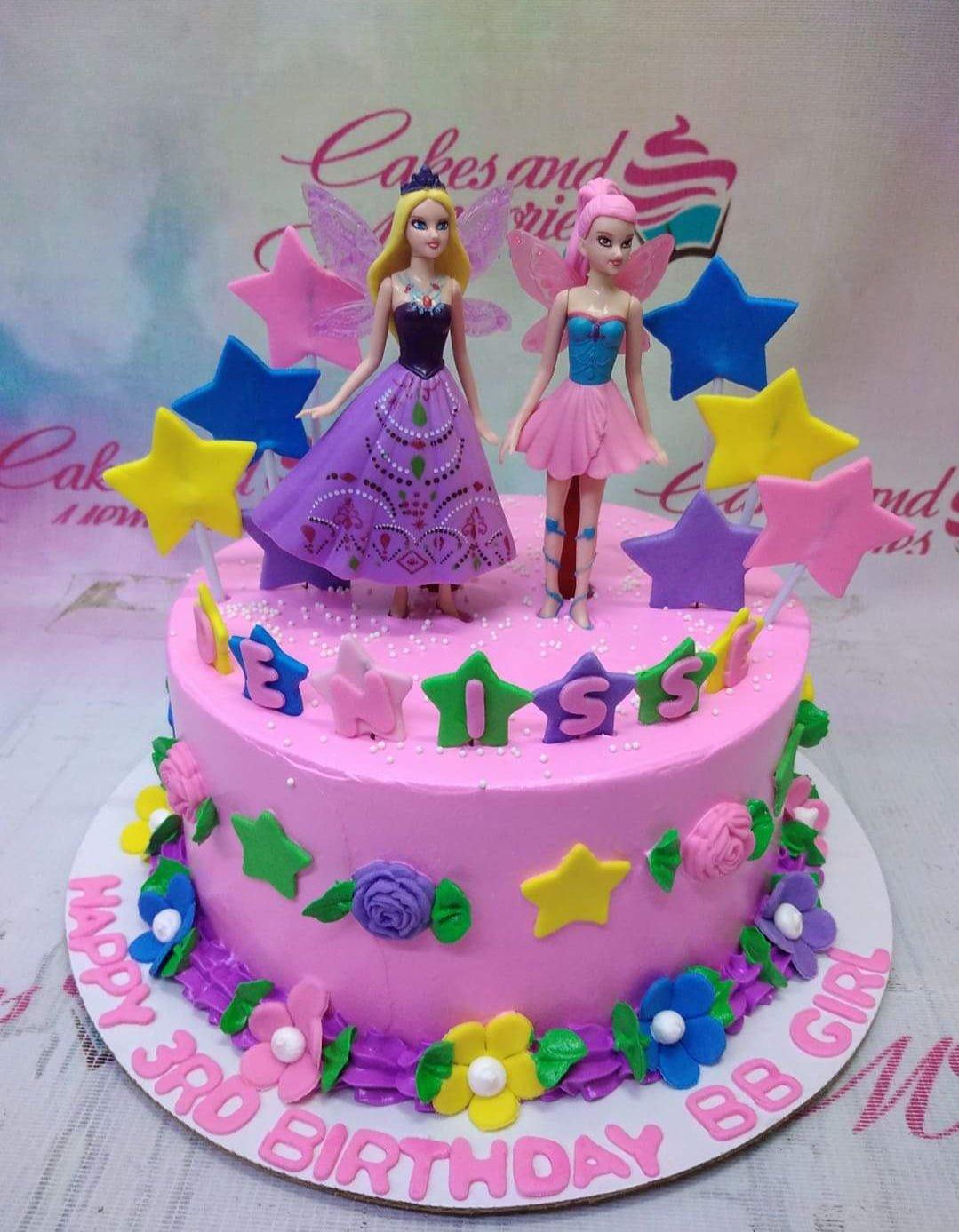 Pink Barbie princess themed cake with two doll toppers, colorful gumpaste stars, and floral icing decorations.