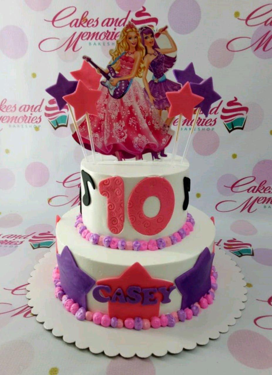 Two-tier Barbie and the Rockstars themed birthday cake in white with pink and purple star decorations and music notes.