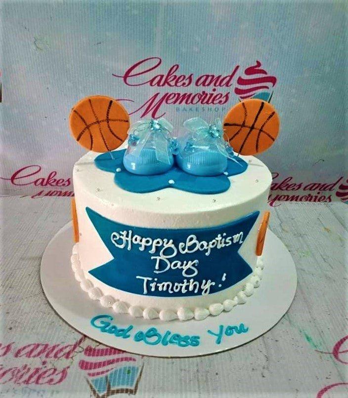 White 1-tier baptism cake with blue basketball and baby shoe toppers, featuring a blue banner with white text.