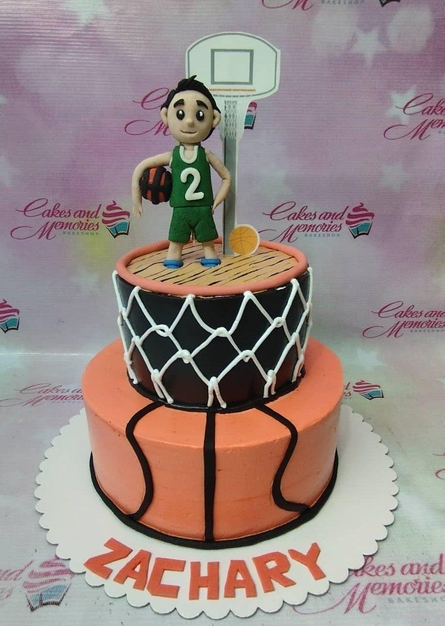 Two-tier basketball themed cake with a 3D basketball player figure, a basketball hoop, and orange basketball-textured icing.