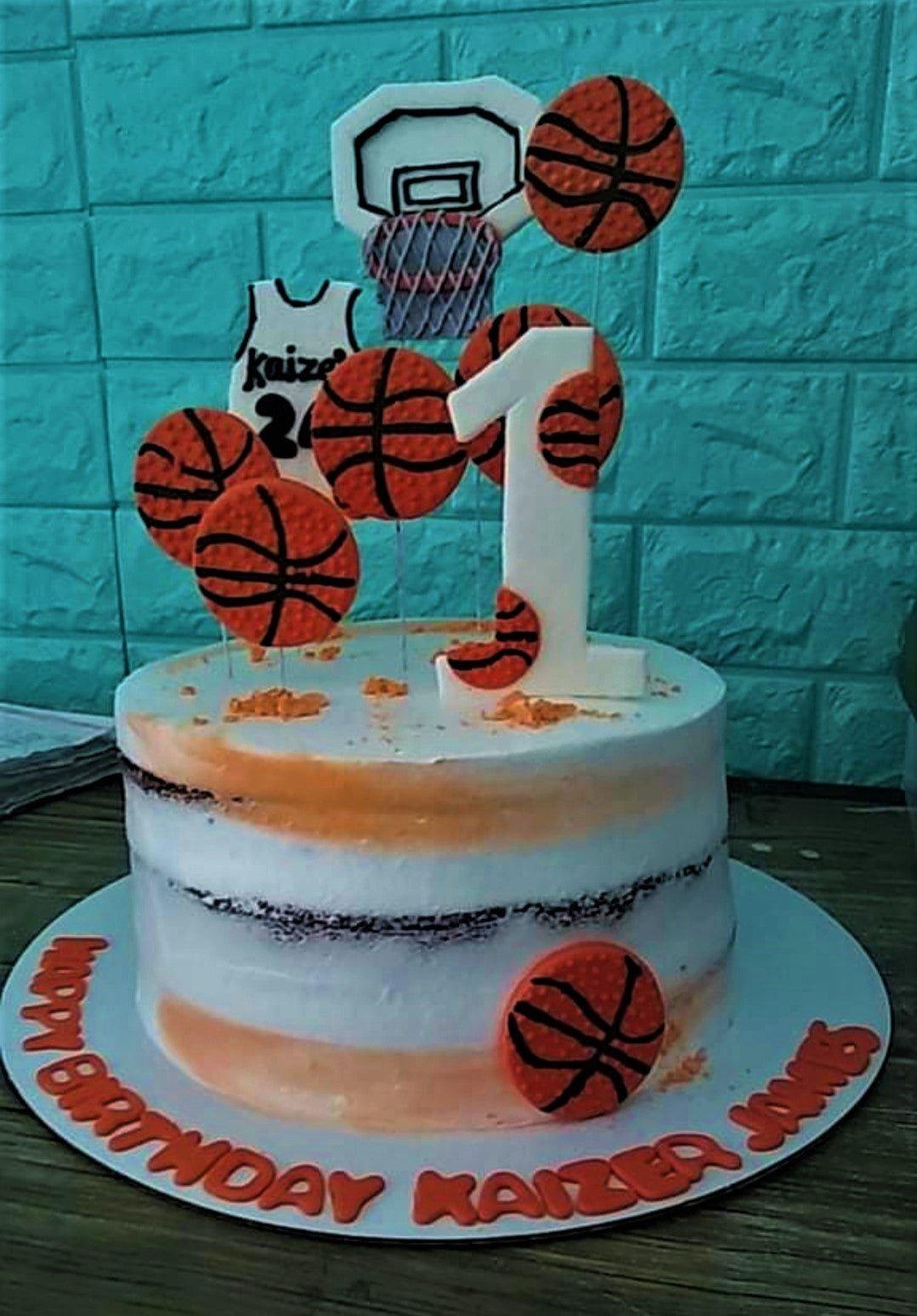 Basketball themed birthday cake with orange basketball toppers, a basketball hoop, and a jersey for Kaizer James.