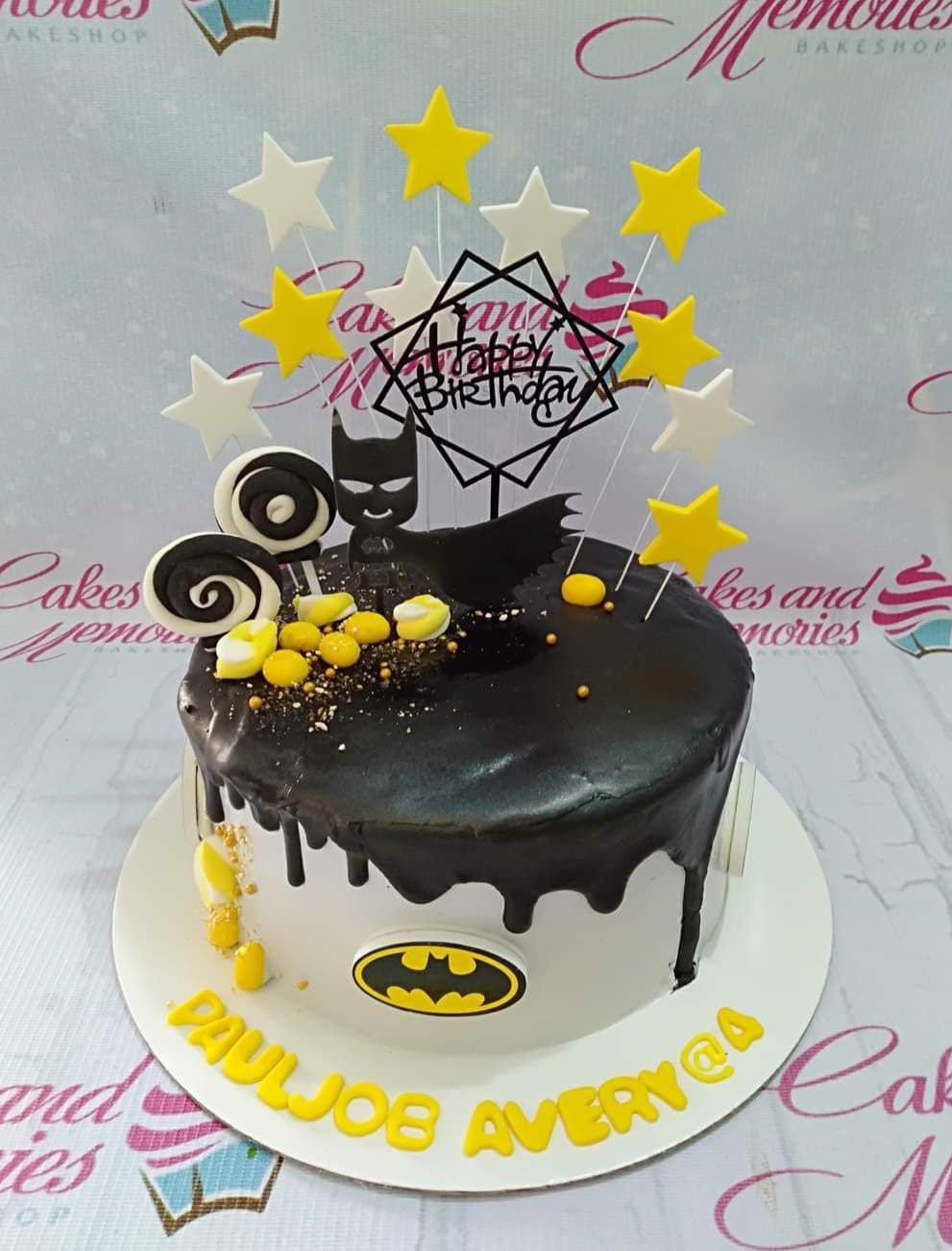 Batman themed birthday cake with black chocolate drip, yellow stars, and a Batman logo on a white base.