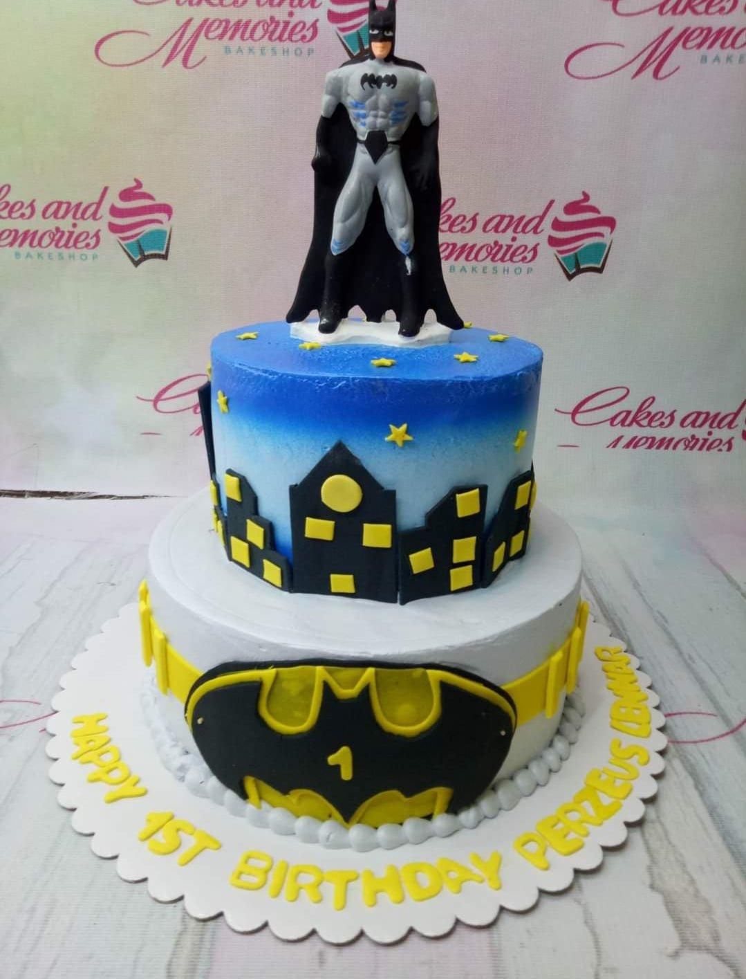 Two-tier Batman themed birthday cake with a Batman figurine on top, city skyline silhouette, and yellow utility belt design.