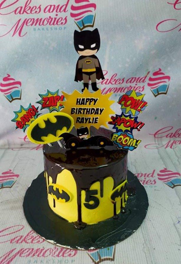 Batman themed birthday cake with yellow icing, chocolate drip, and various Batman character and comic book action word printouts.