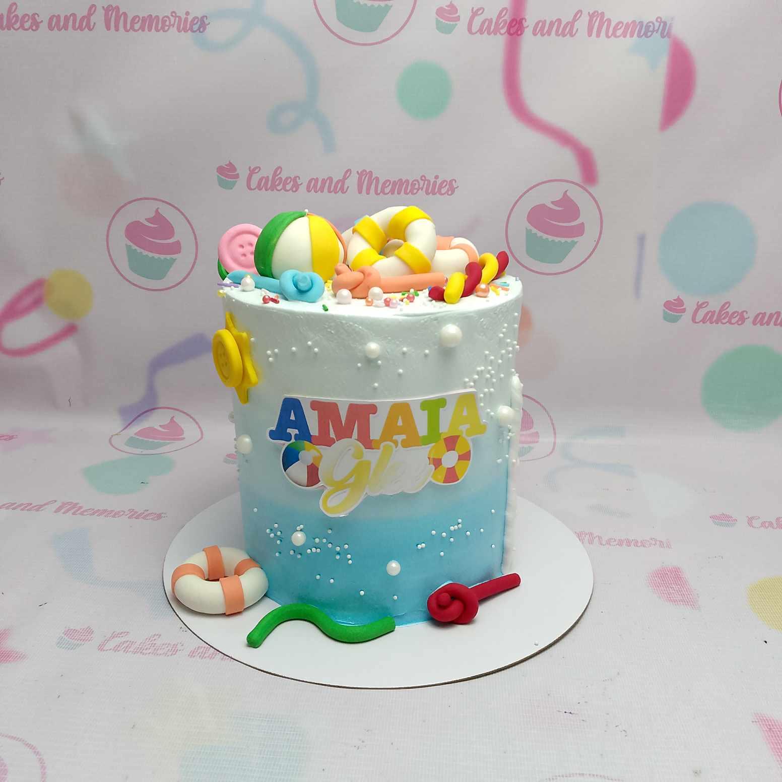 Blue and white gradient beach themed cake with fondant beach balls, life rings, and colorful name topper.