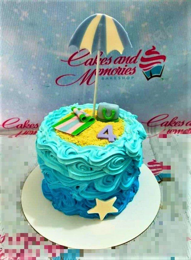 Beach themed birthday cake with blue ombre ruffles, sand icing, a beach umbrella, and a purple number 4 topper.