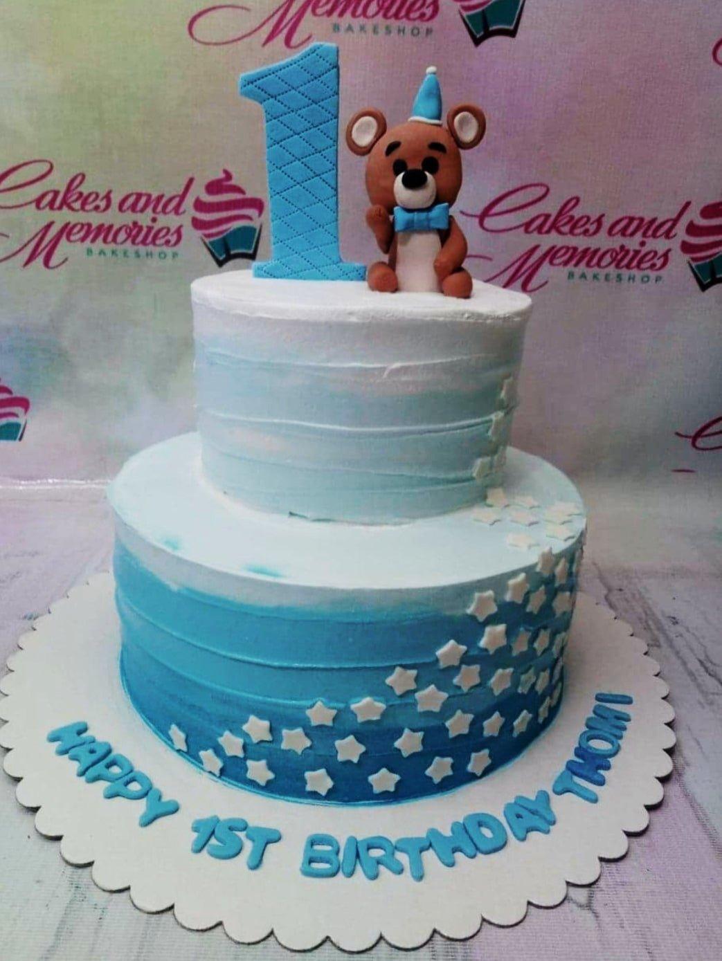 Blue and white 2-tier ombre birthday cake with a fondant bear topper and white stars.