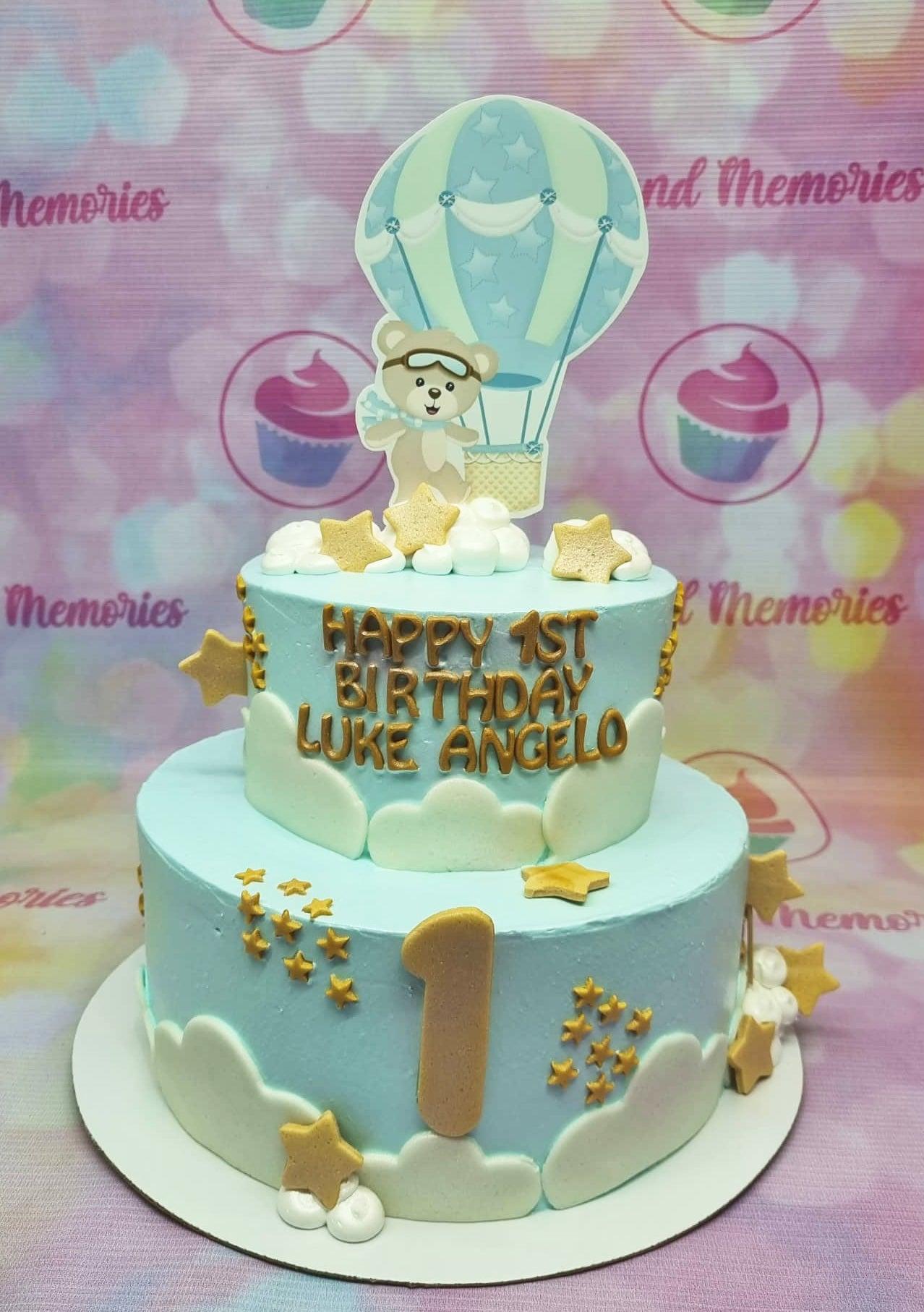 Light blue 2-tier birthday cake with a bear in a hot air balloon topper, white fondant clouds, and gold stars.