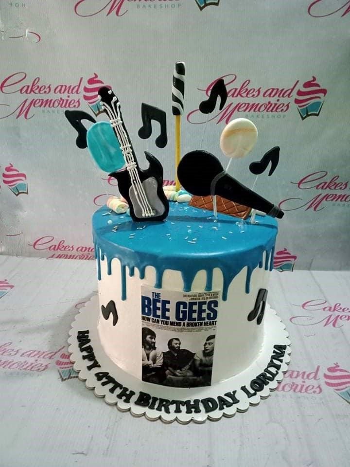Music themed birthday cake with blue drip, guitar, microphone, and Bee Gees album printout for a 47th birthday.