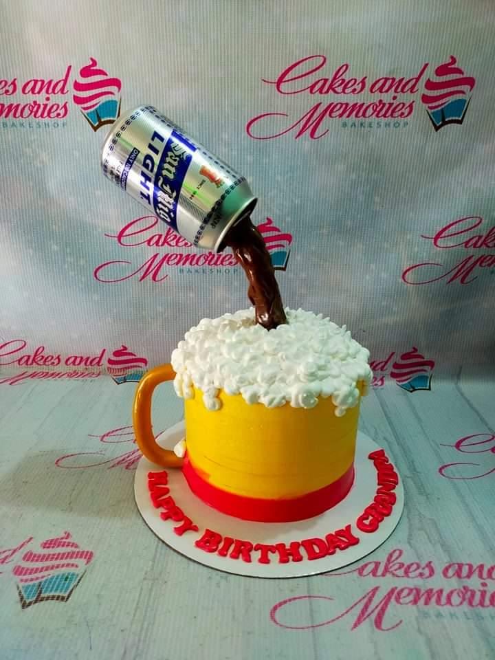 San Miguel Light beer mug cake with a pouring beer can effect and white icing foam on a yellow base.