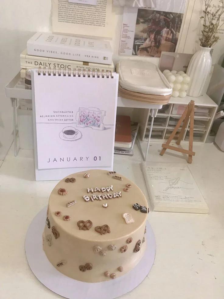 Beige minimalist bento cake with brown and white icing doodles of pretzels, cookies, and toast with Happy Birthday message.